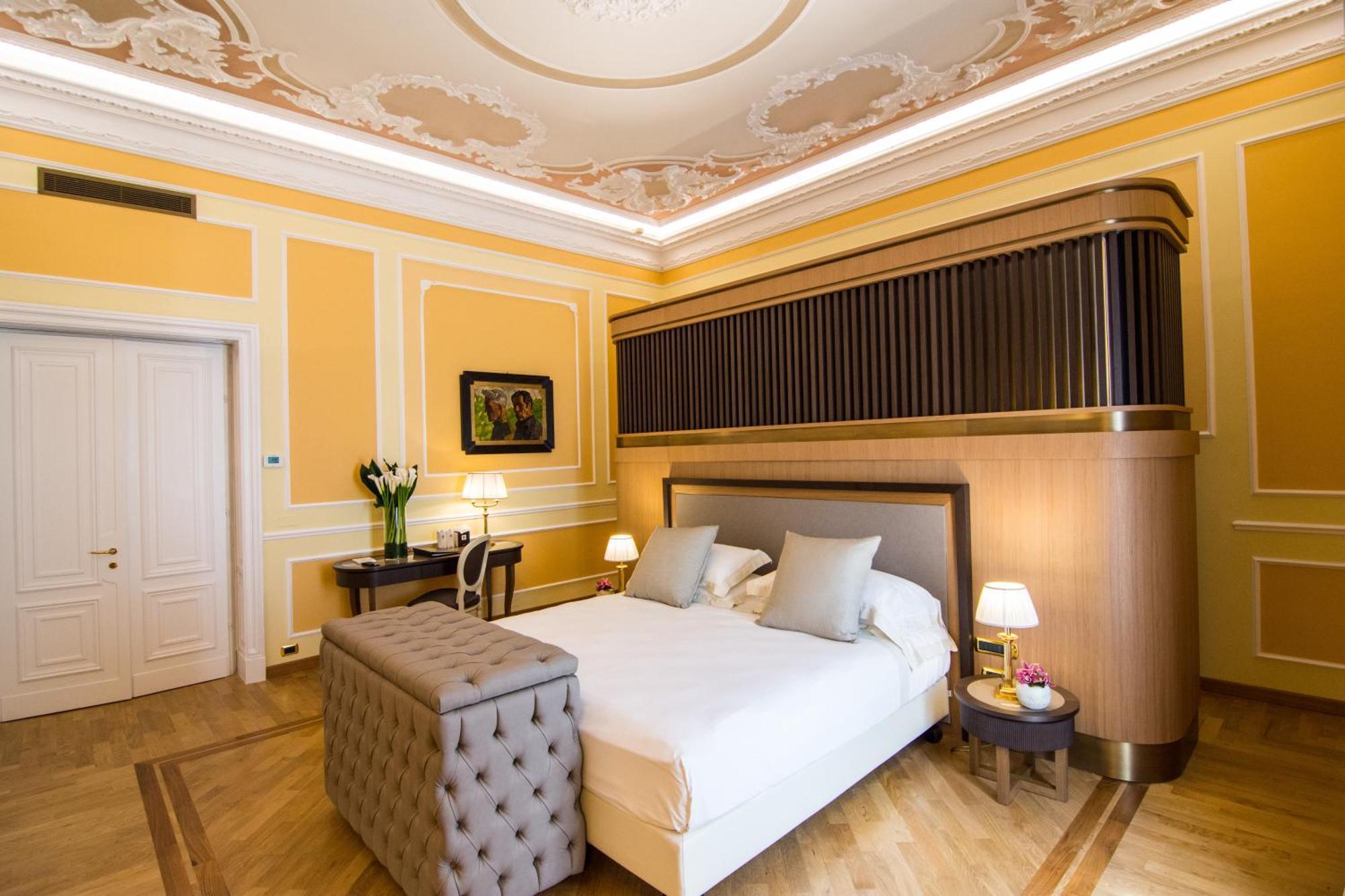 Hotel Bristol Palace Genoa Bagian luar foto The photo shows a beautifully arranged bedroom with elegant decor. The room features warm yellow walls, complemented by intricate molding and a decorative ceiling. In the center, there is a neatly made bed with light-colored bedding and two decorativ