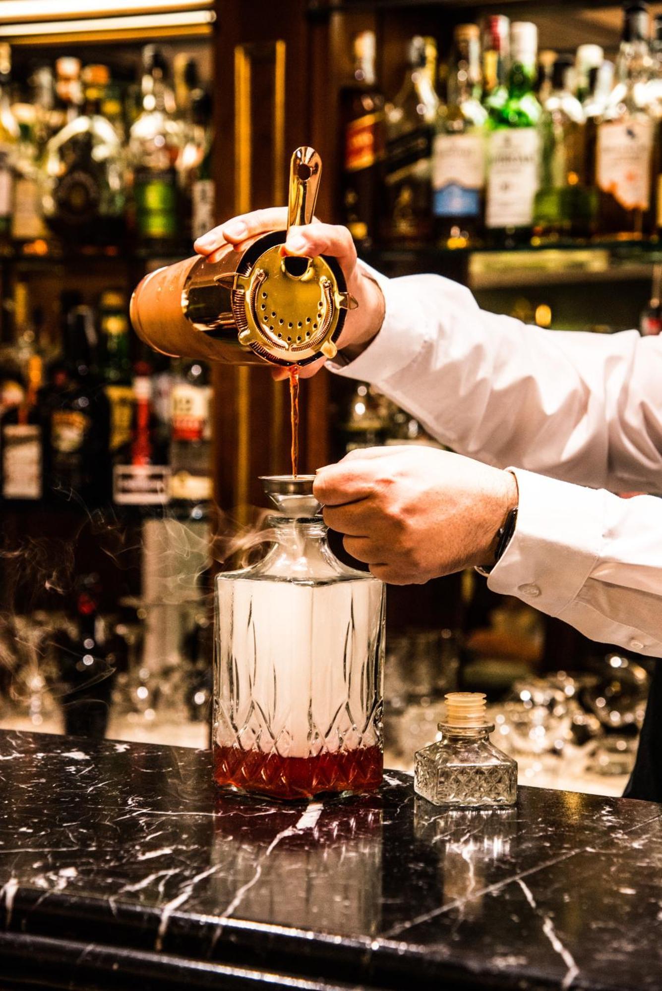 Hotel Bristol Palace Genoa Bagian luar foto The photo shows a bartender pouring a liquid from a cocktail shaker into a glass bottle or decanter. The bartender is holding a strainer over the bottle to catch any solid particles, ensuring a smooth pour. The background displays various bottles of 